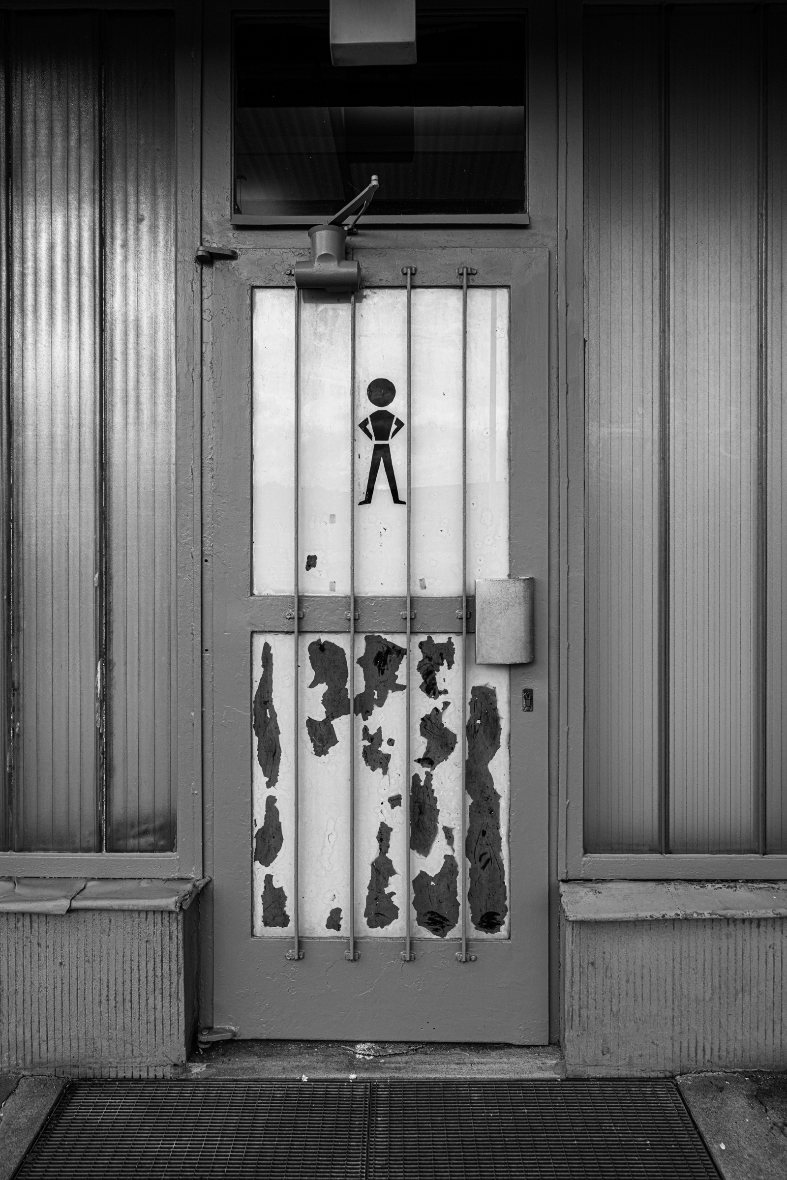 Weathered door with a pictogram and metal bars, Marienborn, 2023