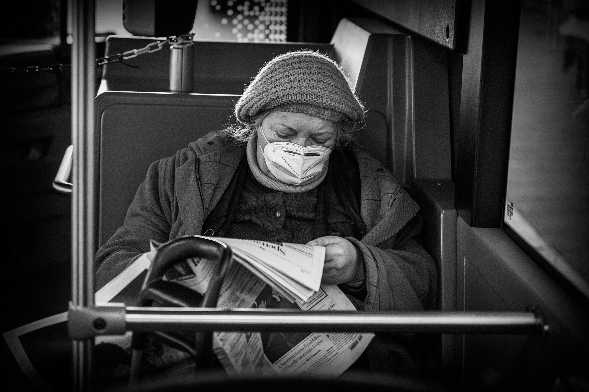 Passenger wearing a knitted hat and face mask, reading a newspaper, Rome, 2023